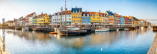 Panorama view of Nyhawn, the colorful houses next to the old port. Tourist visiting restaurants, cafes and ships in the canal at dusk. The most important sightseeing spot in Copenhagen, Denmark.