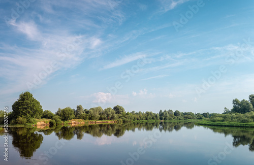 Fototapeta Naklejka Na Ścianę i Meble -  Summer landscape. Calm Berezina river with green banks under a blue sky with clouds.