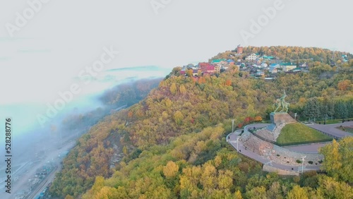 Drone shooting Ufa city: view of the hill with the monument to Salavat Yulaev, autumn forest and thick white fog below, over the river
