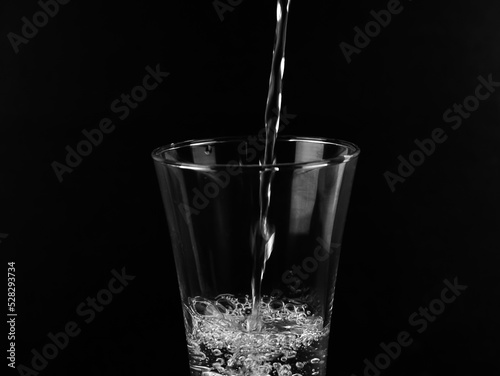 Pouring fresh water on glass on black background. © surasak