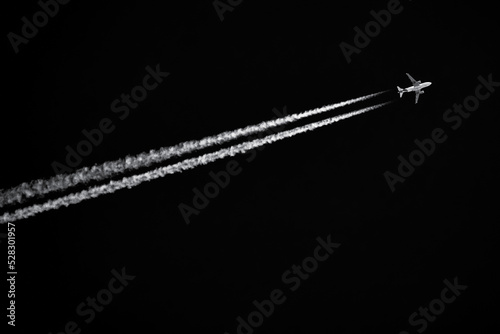 Twin-engined jetliner with contrails flying in black sky photo