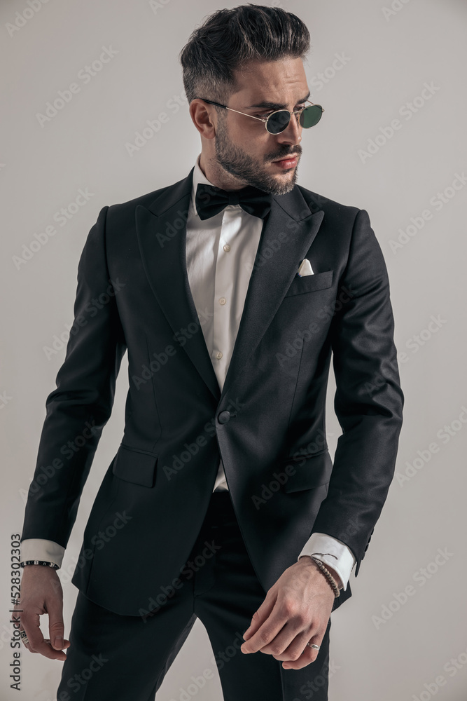 Fototapeta premium elegant groom with sunglasses in black tuxedo looking to side
