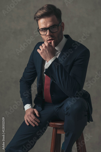 elegant young man in navy blue suit with red tie sitting on wooden chair © Viorel Sima