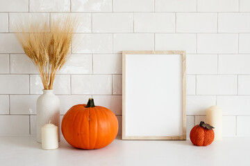 Cozy home interior with frame mockup, autumn fall decorations, pumpkins, vase of wheat, candle. Scandi, minimal style. Poster design for Halloween or Thanksgiving.