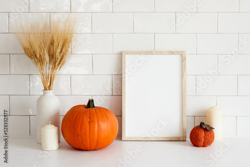 Cozy home interior with frame mockup, autumn fall decorations, pumpkins, vase of wheat, candle. Scandi, minimal style. Poster design for Halloween or Thanksgiving.