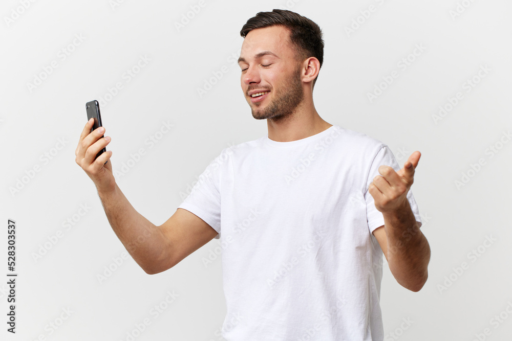 Cheerful smiling tanned handsome man in basic t-shirt talk by video call with friends posing isolated on over white studio background. Copy space Banner Mockup. Distance online communication concept Cheerful smiling tanned handsome man in basic t-shirt talk by video call with friends posing isolated on over white studio background. Copy space Banner Mockup. Distance online communication concept