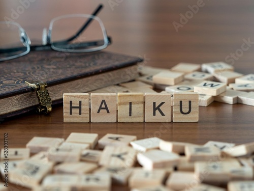 haiku word or concept represented by wooden letter tiles on a wooden table with glasses and a book photo