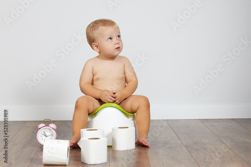 Cute baby boy sits on the potty with toilet paper in his hands. Potty training time photo