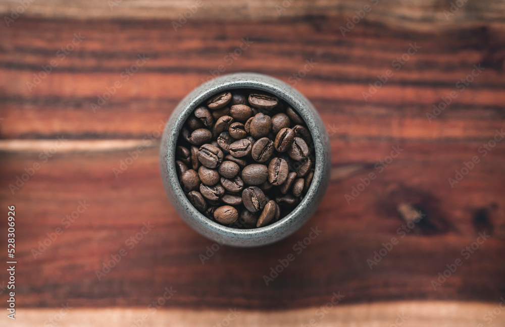 Roasted coffee beans in a cup on a wooden surface - top view Roasted coffee beans in a cup on a wooden surface - top view