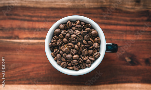 Roasted coffee beans in a cup on a wooden surface - top view