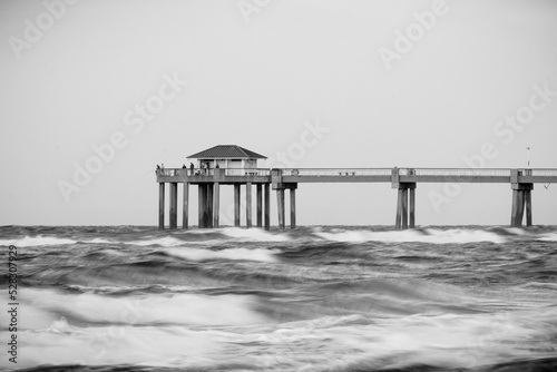 Long exposure view of a concrete pier on an overcast day with wavy water in front of it. 