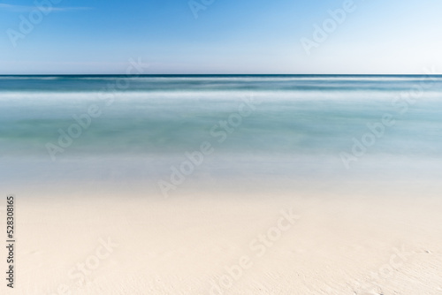 Fototapeta Naklejka Na Ścianę i Meble -  Long exposure of a beach on the Gulf of Mexico. The water is blue with golden sand and a blue sky. 