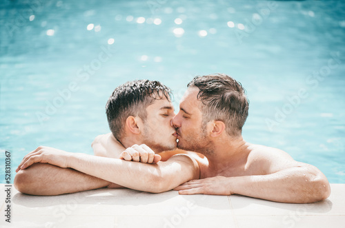 Gay couple relaxing in swimming pool. LGBT. Two young men enjoying nature outdoors, kissing and hugging. Young men romantic family in love. Happiness concept. 