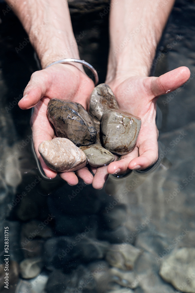 Man showing the stones he holds in his hand over a small lake.