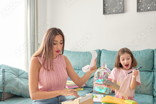 mother and daughter sitting on the sofa at home. Daughter very happy with her school materials and mother worried about what she has spent buying them and the rise in prices