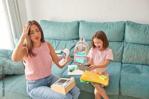 mother and daughter sitting on the sofa at home. Daughter very happy with her school materials and mother worried about what she has spent buying them and the rise in prices