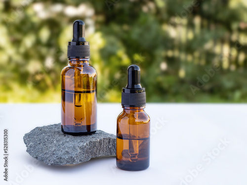 Two brown bottles of essential oil, essence, serum for women's skin care on a natural background. Stone podium. Front view