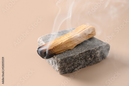 Palo Santo stick incense burning on gray stone on beige background. . Ritual cleansing, meditation, aromatherapy for relax. Close up.