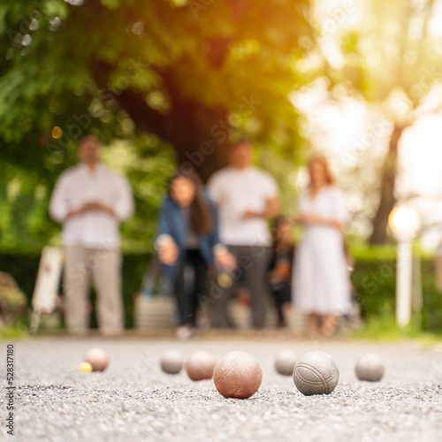 Group of friends playing bocce game woman through a ball above green trees park in city park in summer sunset light
