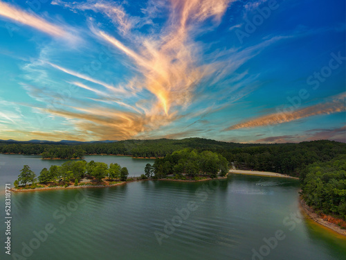 an aerial shot of a gorgeous summer landscape on the lake with rippling green water surrounded by lush green trees, grass and plants with powerful clouds at sunset at Red Top Mountain State Park photo