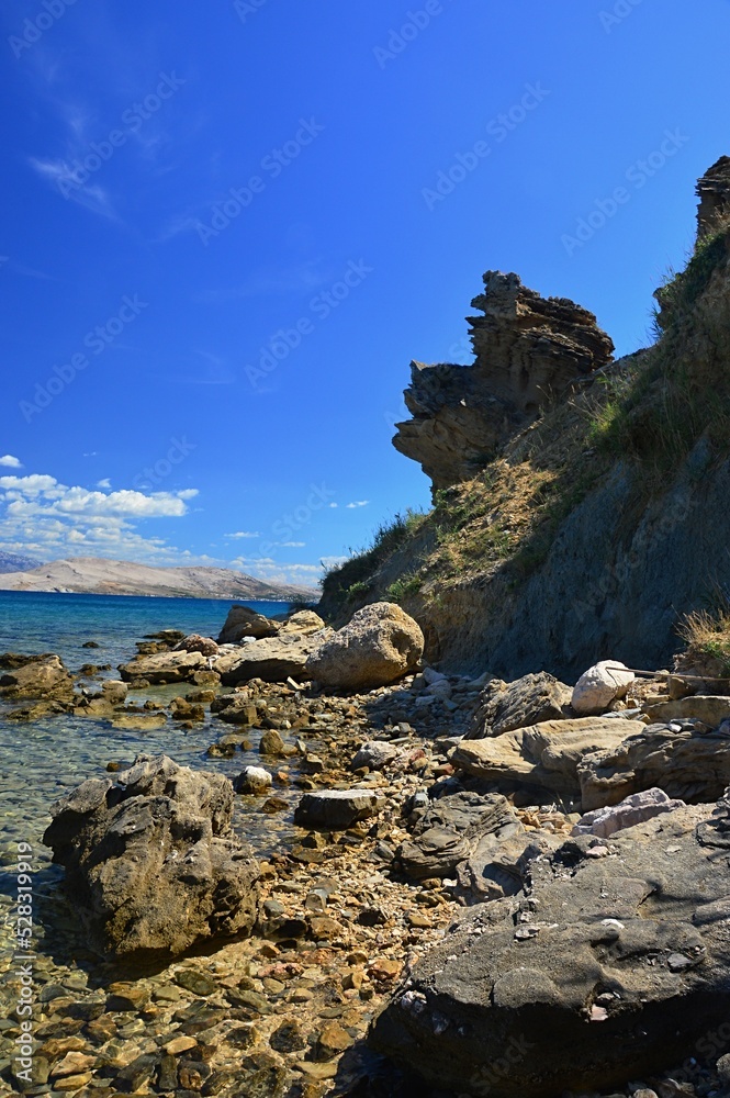 Arid sharp eroded shoreline rock with some foliage of grass and small shrubs on Pag island, Sveta Maria beach, northern Dalmatia, Croatia. Blue summer skies with some clouds.