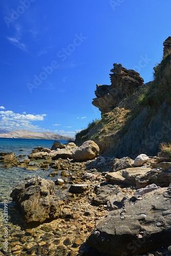 Arid sharp eroded shoreline rock with some foliage of grass and small shrubs on Pag island, Sveta Maria beach, northern Dalmatia, Croatia. Blue summer skies with some clouds.