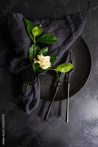 Overhead view of a black place setting on a table with a white gardenia flower photo