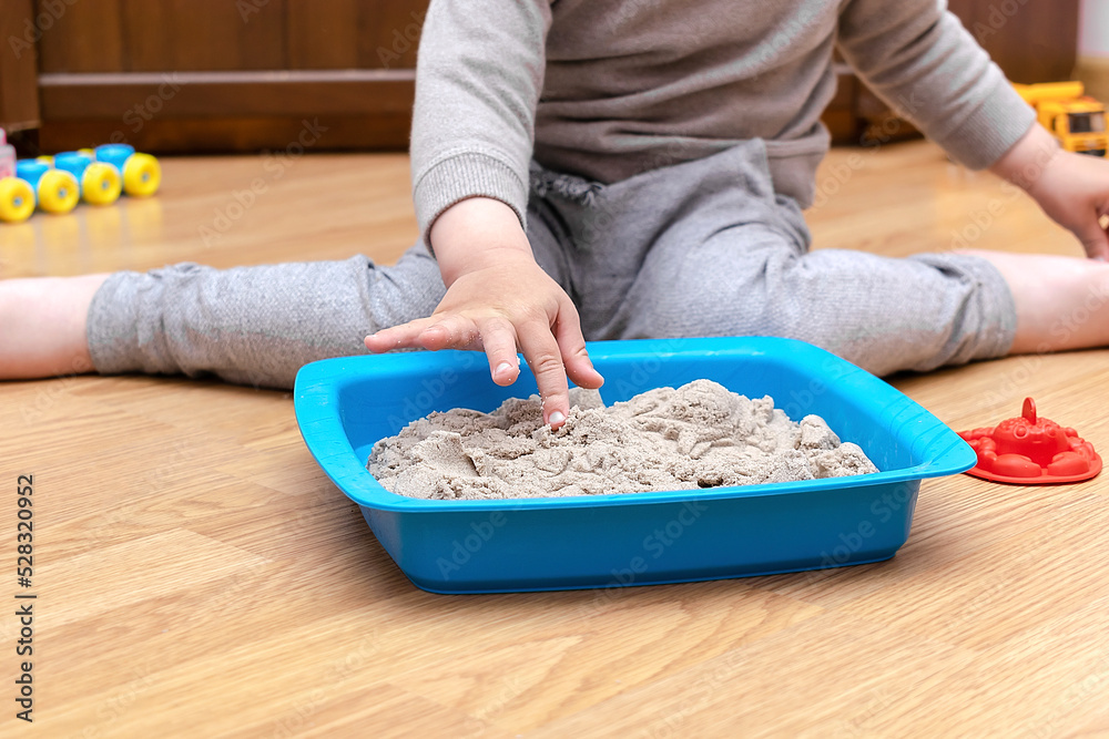 little child boy playing at home in sensory box with kinetic sand.Development of fine motor skills. Early sensory education. Activities Montessori.art creativity, craft at daycare,kindergarten little child boy playing at home in sensory box with kinetic sand.Development of fine motor skills. Early sensory education. Activities Montessori.art creativity, craft at daycare,kindergarten