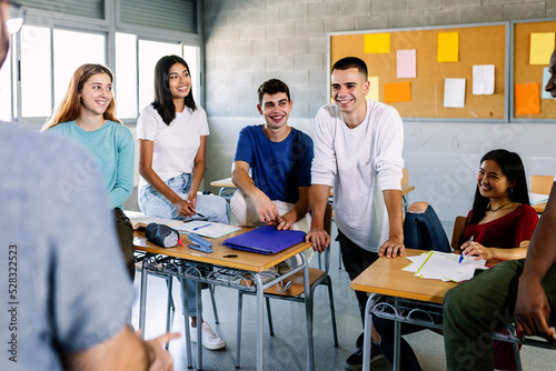 Male teacher and teenage young students talking during a break in classroom - Happy group of diverse millennial people hanging out with tutor in high school