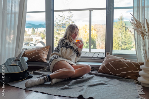 Woman in knitted wool sweater drinks tea a cup, relax at home in winter day. Health care, authenticity, sense of balance and calmness. Fresh air.