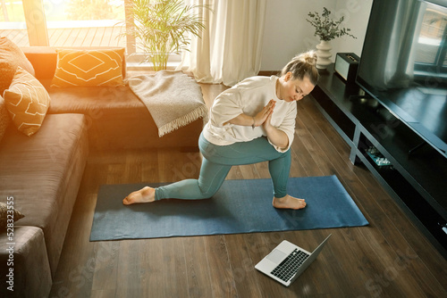 Woman doing online yoga at home. Female trener teaches asana in video conference. Health care, authenticity, sense of balance and calmness.