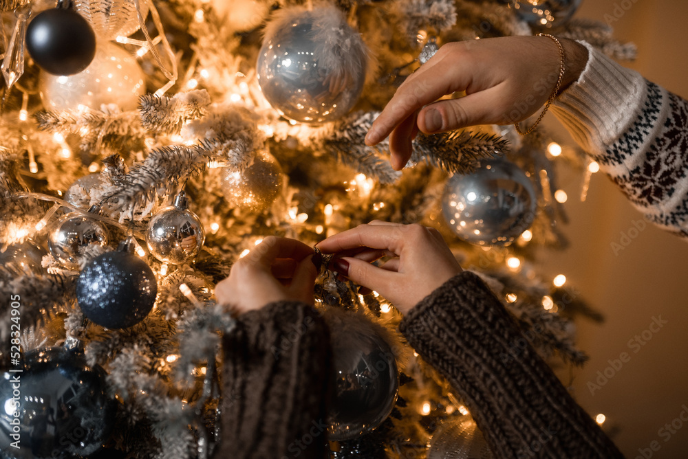 close-up of the hands of a man and a woman decorate the Christmas tree with balls