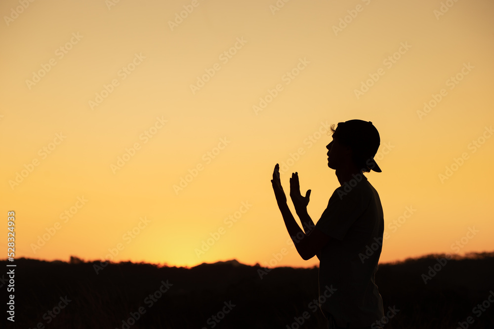 Silhouette of a man praying and thanking God with the sunset sky in the background. Receiving God's blessing.