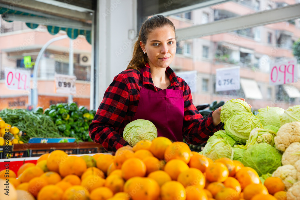 Obraz premium Portrait of a positive girl of the seller in the store laying out cabbages on the counter