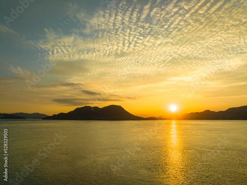 Sunrise reflects off calm seas against silhouetted coastal background