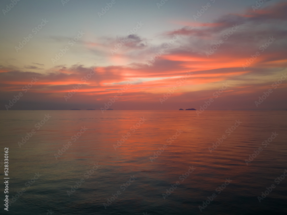 Sunrise reflects off clouds and calm ocean waters with small island in background