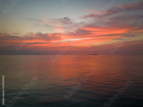 Sunrise reflects off clouds and calm ocean waters with small island in background