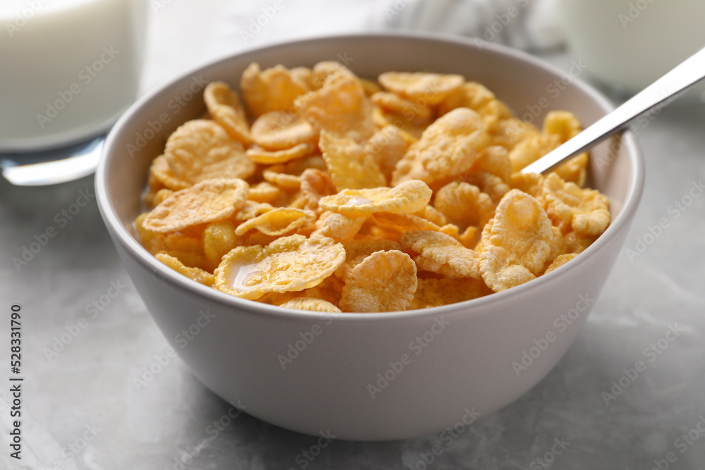 Spoon in bowl with tasty cornflakes and milk on light grey table, closeup Spoon in bowl with tasty cornflakes and milk on light grey table, closeup