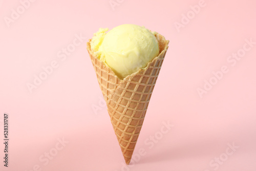 Delicious yellow ice cream in waffle cone on pink background
