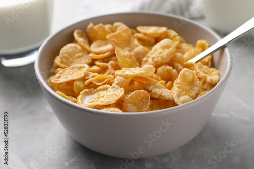 Spoon in bowl with tasty cornflakes and milk on light grey table, closeup