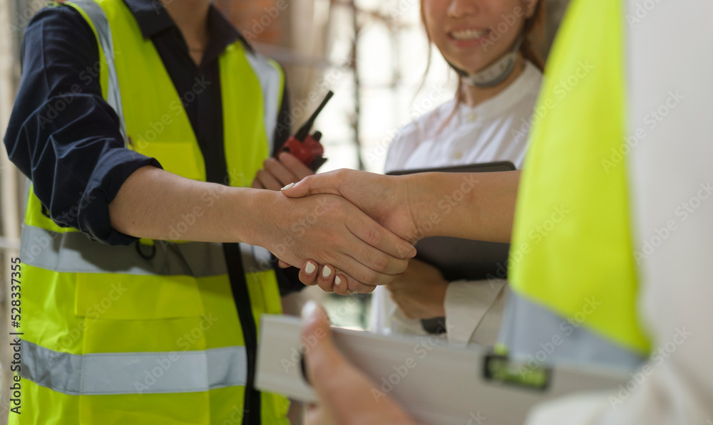 Engineers in yellow vests shaking hands while working at construction site. Building construction collaboration concept.