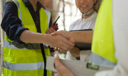 Engineers in yellow vests shaking hands while working at construction site. Building construction collaboration concept.