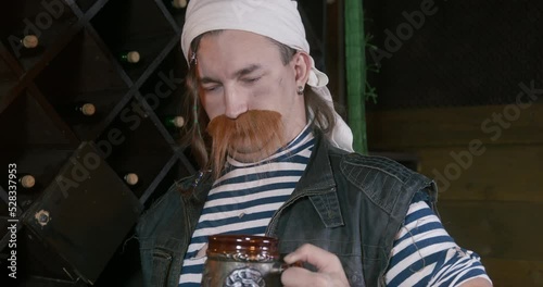 Sailor in bandana with mug in his hand is too drunk trying to make toast. Man in wine cellar tasting drinks and trying to make speech. Drunkard with beer in his hand in tavern, bar. Feast of pirates i photo