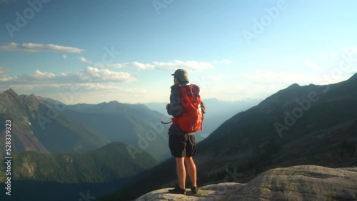 Caucasian man on hiking trip walks out to cliff edge to view epic mountain landscape