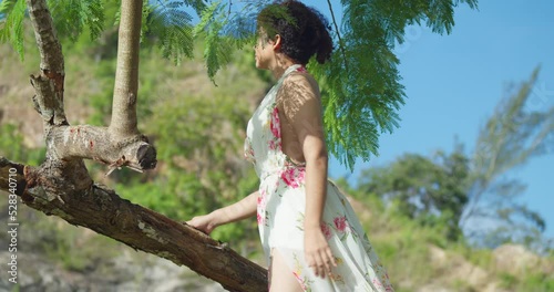 Low angle view of a red hair latina standing on a tree trunk in a long flower dress at a park photo