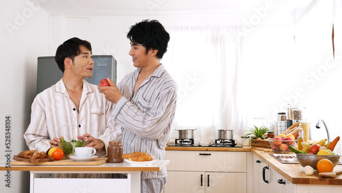 Happy gay couple enjoy breakfast in kitchen drinking coffee. Two best friends LGBTQ relation partner home cooking. Happiness romance homosexual marriage lifestyle. Two men together love friendship.