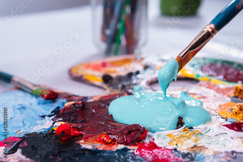 High quality photography. Palette full of paint with a brush taking it. Blue paint in a color palette. Artist materials working with acrylic paints.