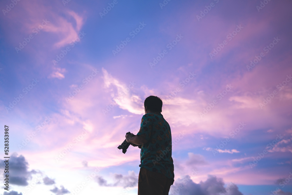 Silhouette rear view of adult travel asian photographer man with camera under the beautiful dramatic sunset sky