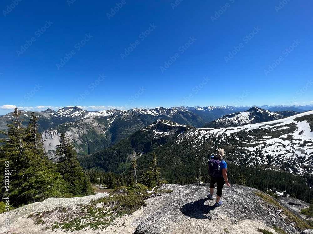 Woman hiking overlooking valley and mountains with forests below her from peak .