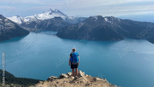 Woman with backpack overlooking big Canadian glacier fed lake with snow capped mountains in the background 